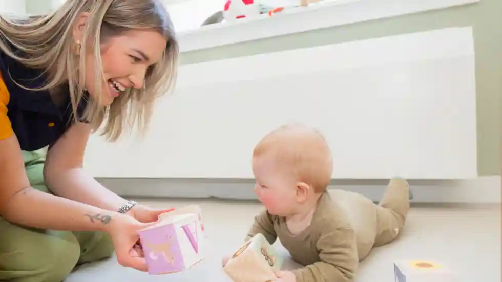 OuderKindgroepen van gro-up Een pedagogisch medewerker speelt met een baby die over de grond kruipt op een ouder-kindgroep van gro-up