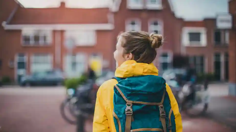 Terug Naar School Zo Help Je Je Kind Weer In Het Ritme Te Komen meisje met een gele jas en een rugtas loop op straat