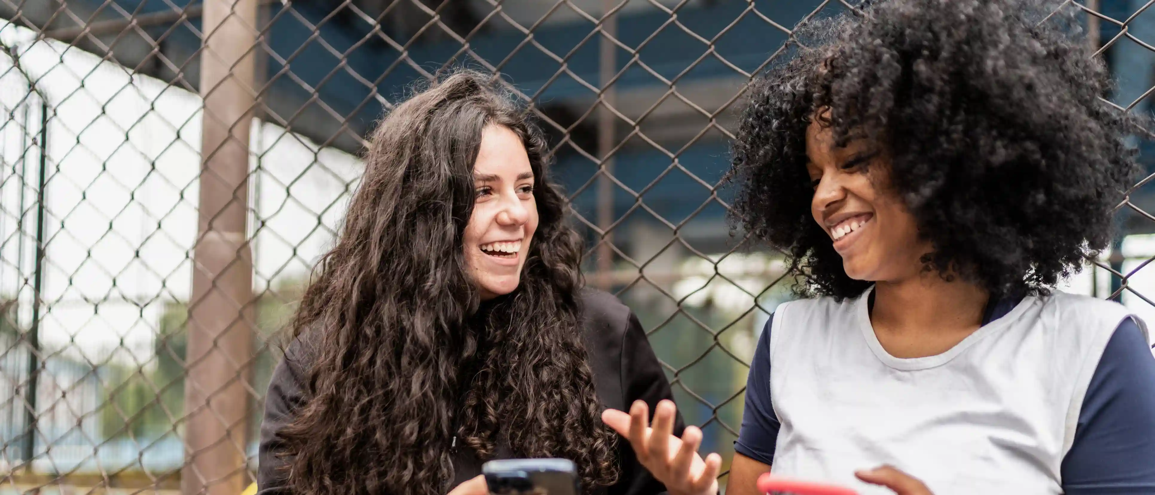 Wat Is Meidenvenijn Twee meisjes lachen met elkaar met een smartphone in de hand
