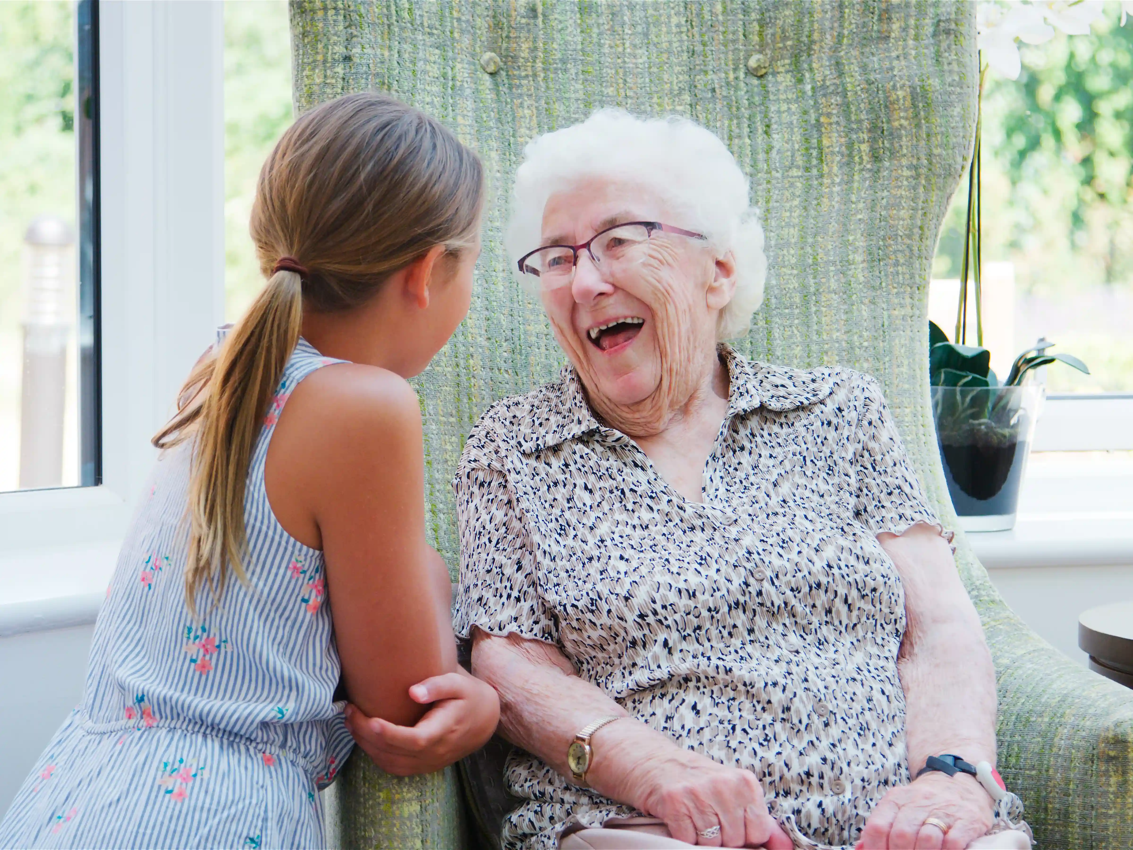Positieve gezondheid voor ouderen van gro-up Oudere dame lacht om haar kleindochter die aan haar stoel staat