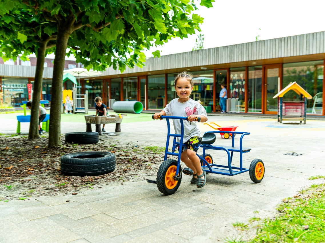 gro-up Een meisje fietst op een driewieler op de binnenplaats van gespecialiseerde kinderopvang Gulliver in Wateringse Veld