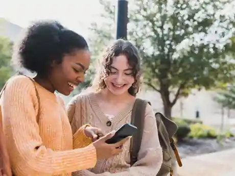 Online Jongerenwerk Twee tienermeisjes lachen naar iets wat een van de meisjes op haar smartphone ziet