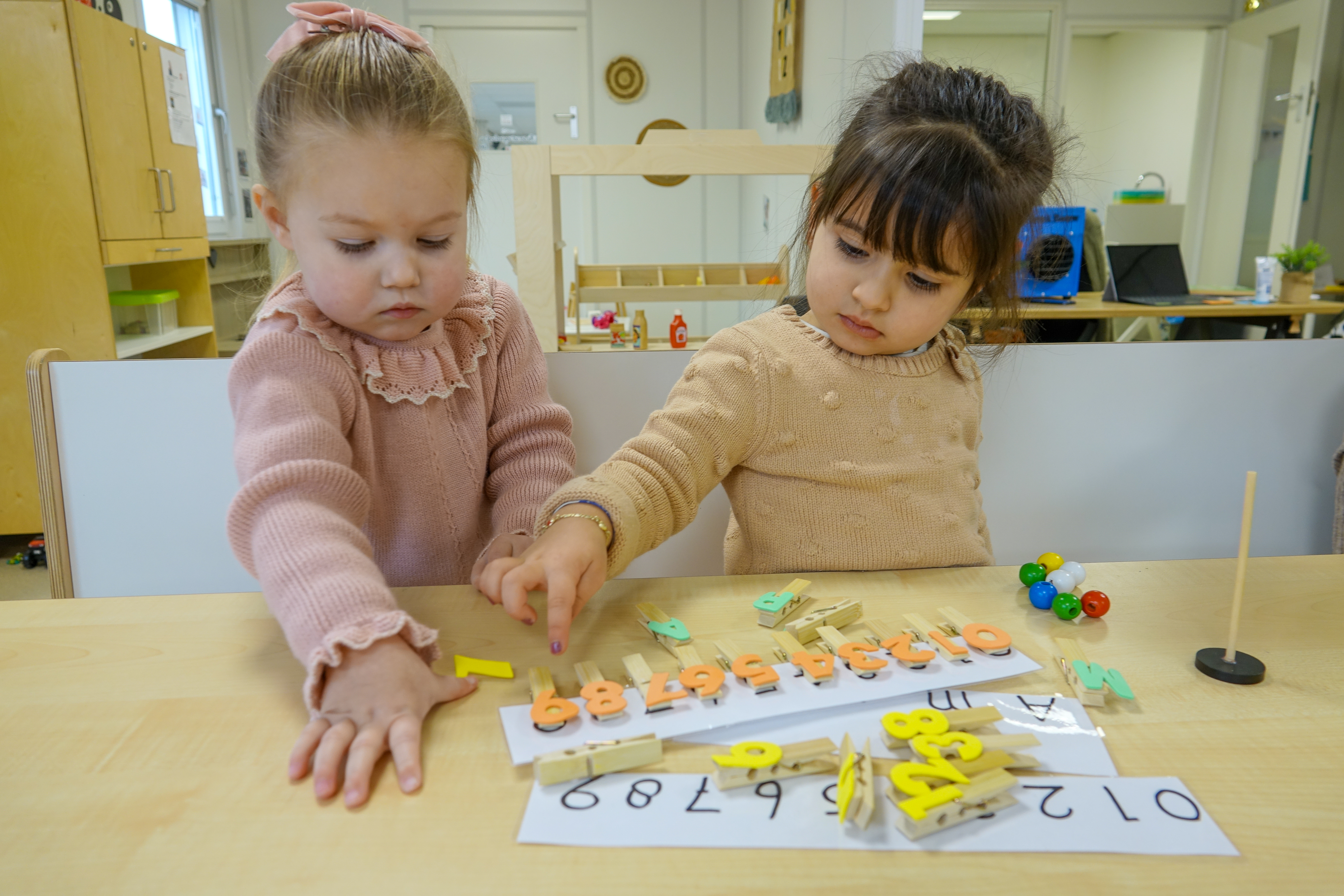 Twee meisjes spelen met wasknijpers met cijfers erop en leren zo tellen bij peuteropvang Het Spectrum van gro-up