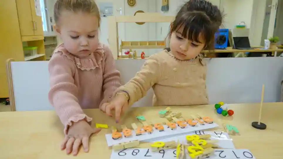 po Het Spectrum van gro-up Twee meisjes spelen met wasknijpers met cijfers erop en leren zo tellen bij peuteropvang Het Spectrum van gro-up