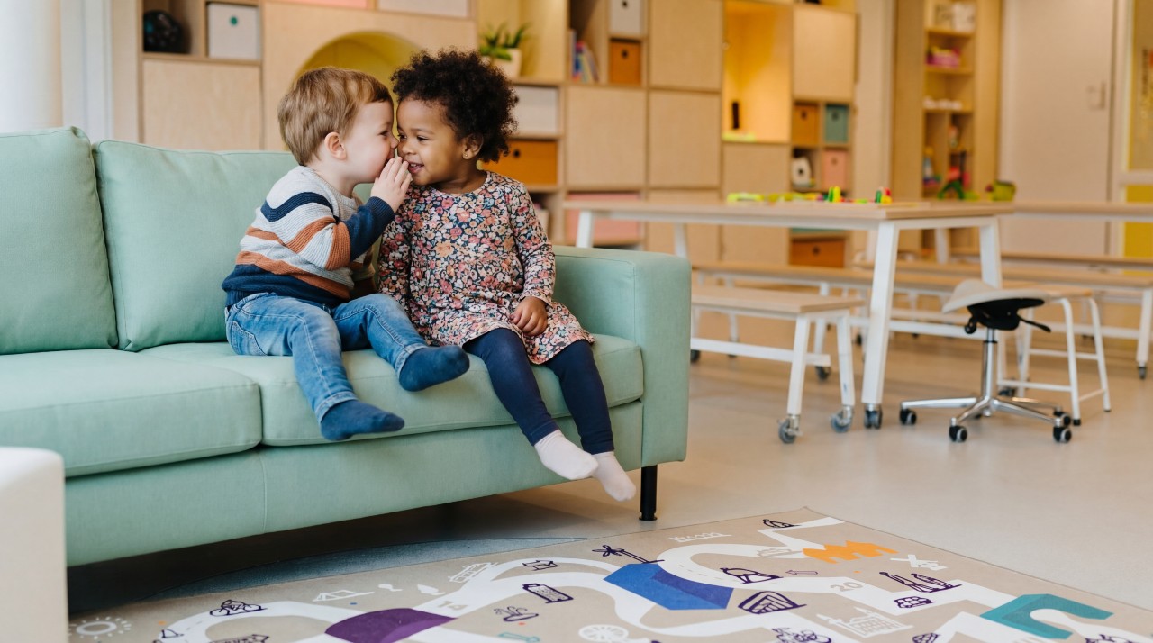 gro-up kinderen Twee peuters, een jongen en een meisje, fluisteren met elkaar op een bank op een peuteropvang