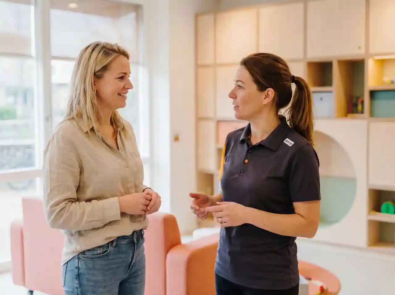 Een pedagogisch professional leidt een moeder rond op de kinderopvang van gro-up