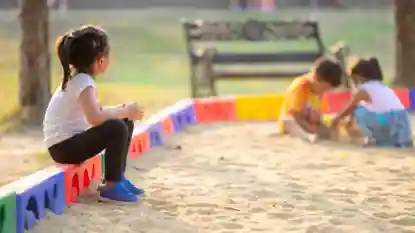 gro-up kind in zandbak kijkt naar spelende kinderen