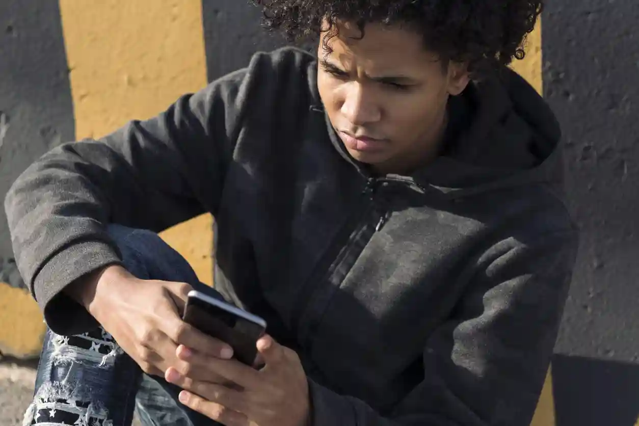 gro-up jeugd Tiener jongen leest nieuws op zijn telefoon terwijl hij buiten tegen een muur aanzit
