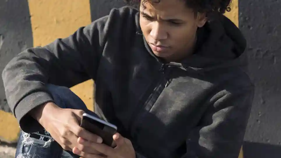 Je Kind Geruststellen Bij Heftig Nieuws Zo Doe Je Dat Samen Tiener jongen leest nieuws op zijn telefoon terwijl hij buiten tegen een muur aanzit