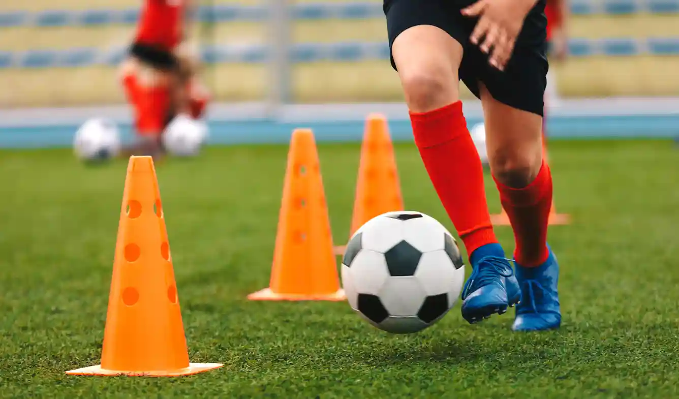 Feyenoord Geeft Training Aan Oekraïense Kinderen Een kind dribbelt met een voetbal lang pionnen op een voetbalveld
