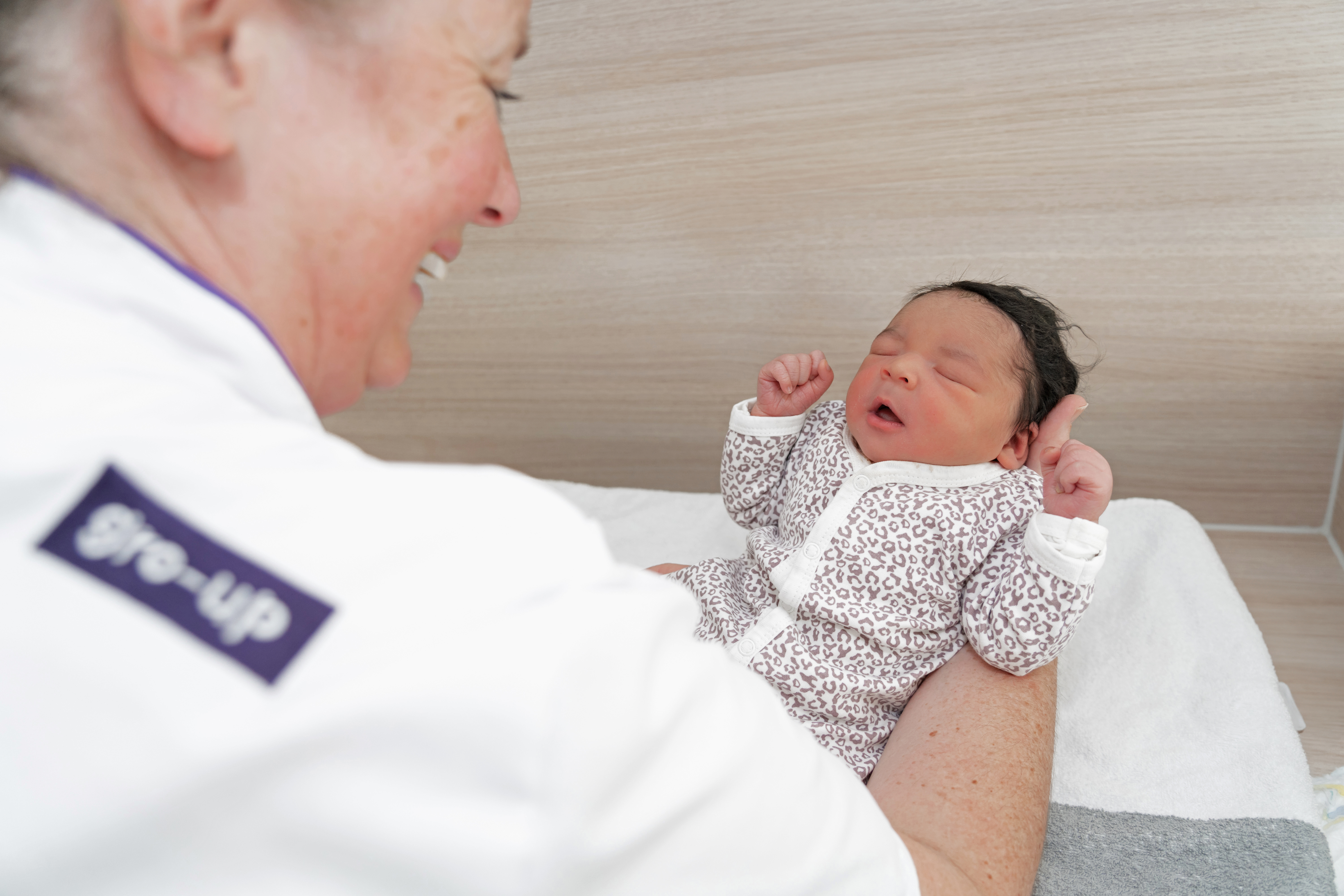 Een kraamverzorgende van gro-up tilt een baby op in gro-up Kraamzorghotel Noord