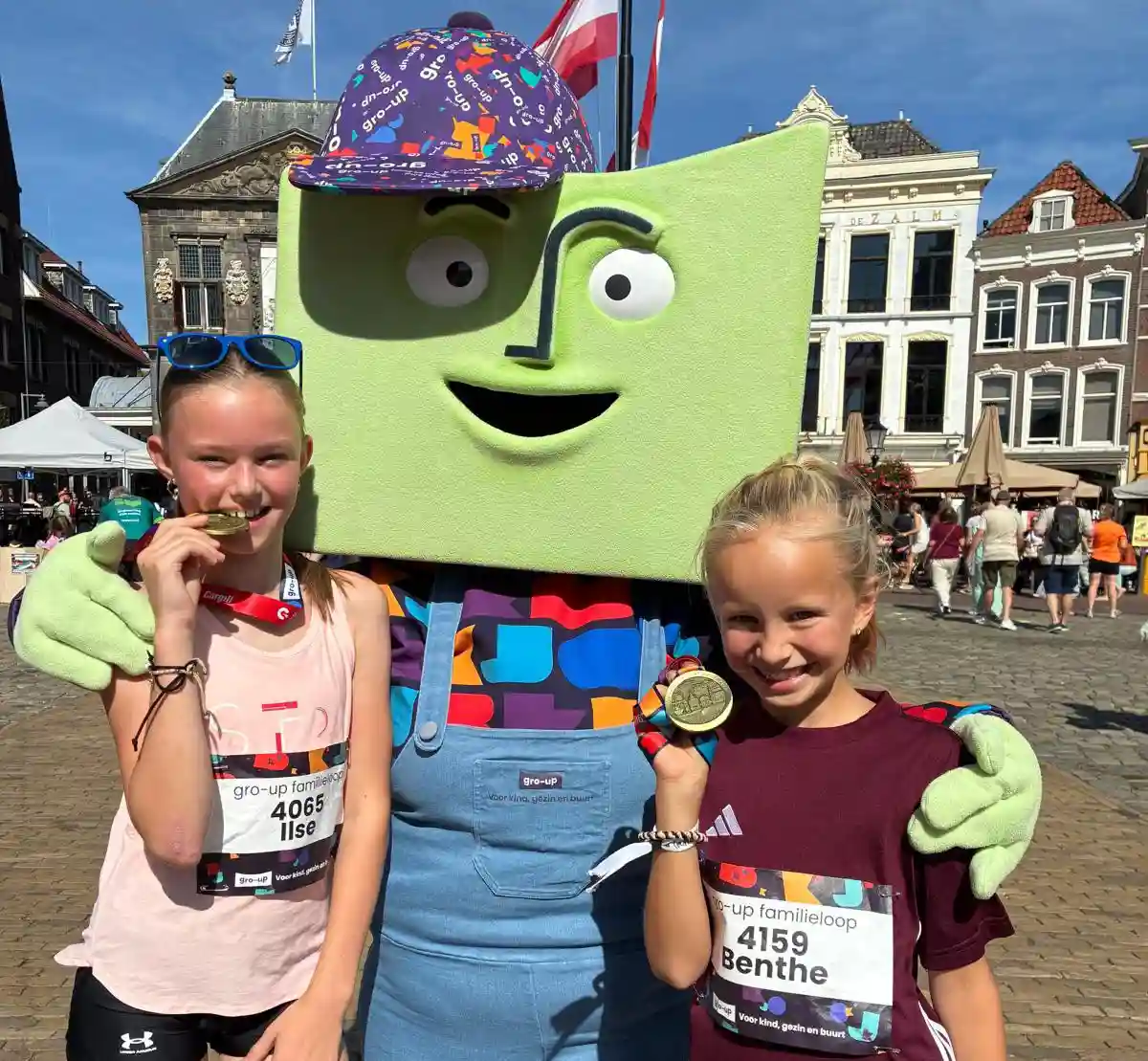 Twee meisje poseren trots met hun medaille en mascotte grup tijdens de gro-up Familie Loop Dordrecht 