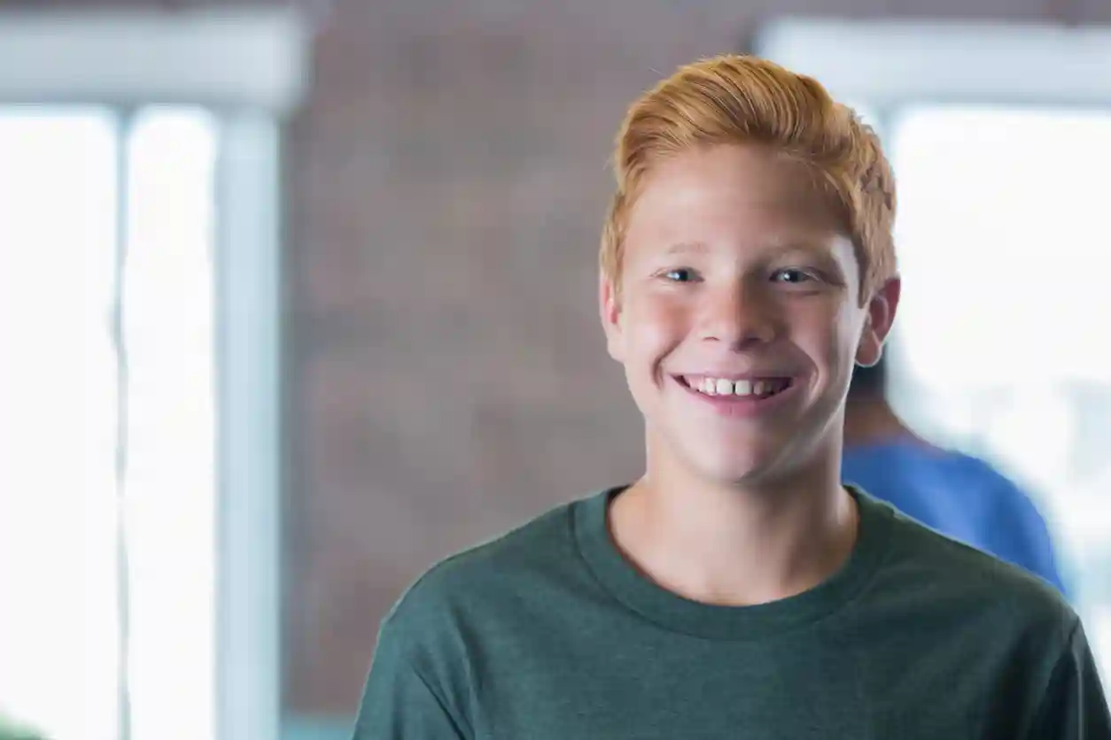 Schooljongerenwerk Rossige jongen kijkt lachend in de camera op school