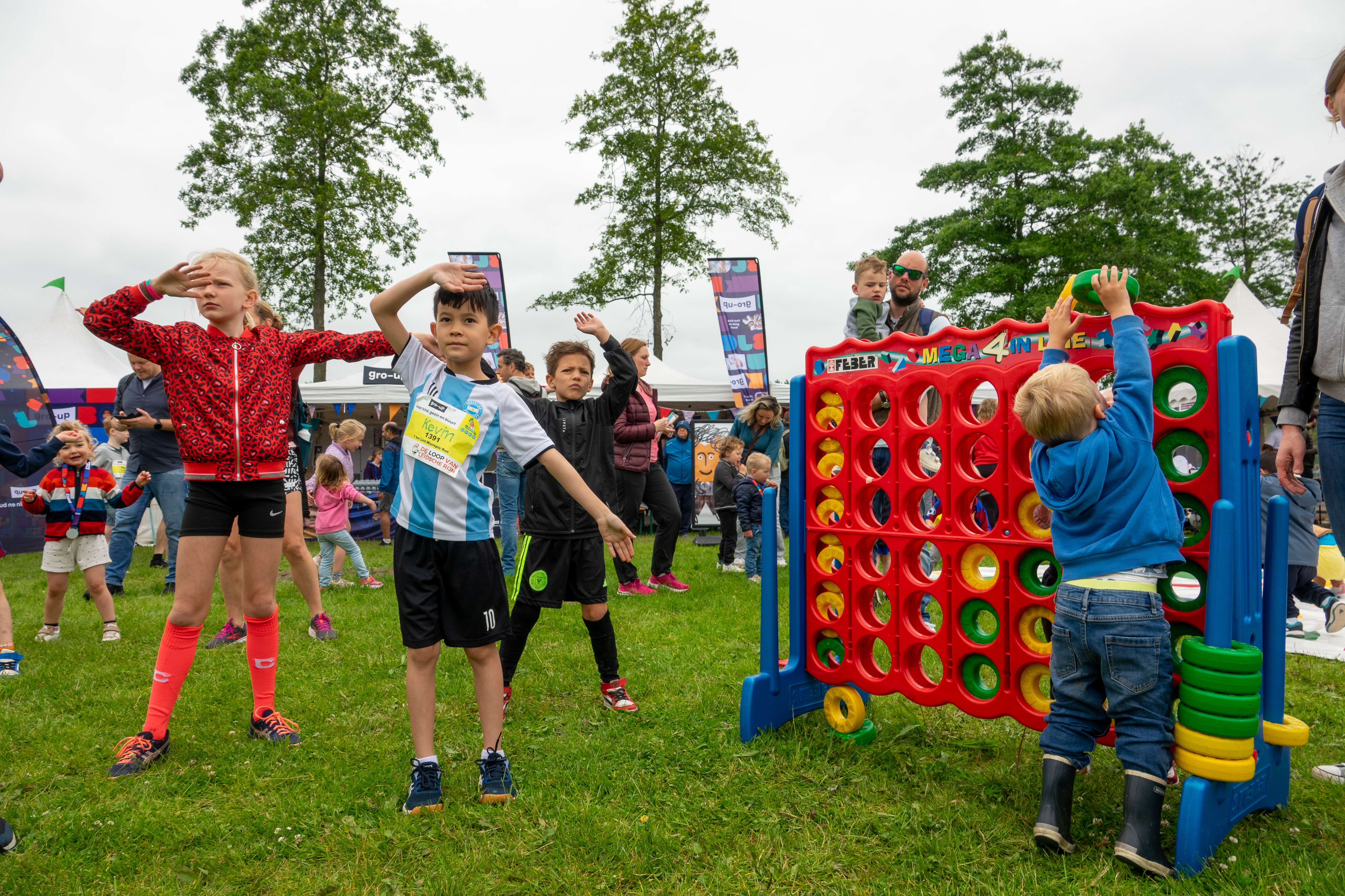 Kinderen doen een warming-up terwijl een jongetje spelen levensgroot vier-op-een-rij speelt in de kids corner tijdens de gro-up Lint-Wurmpie Run